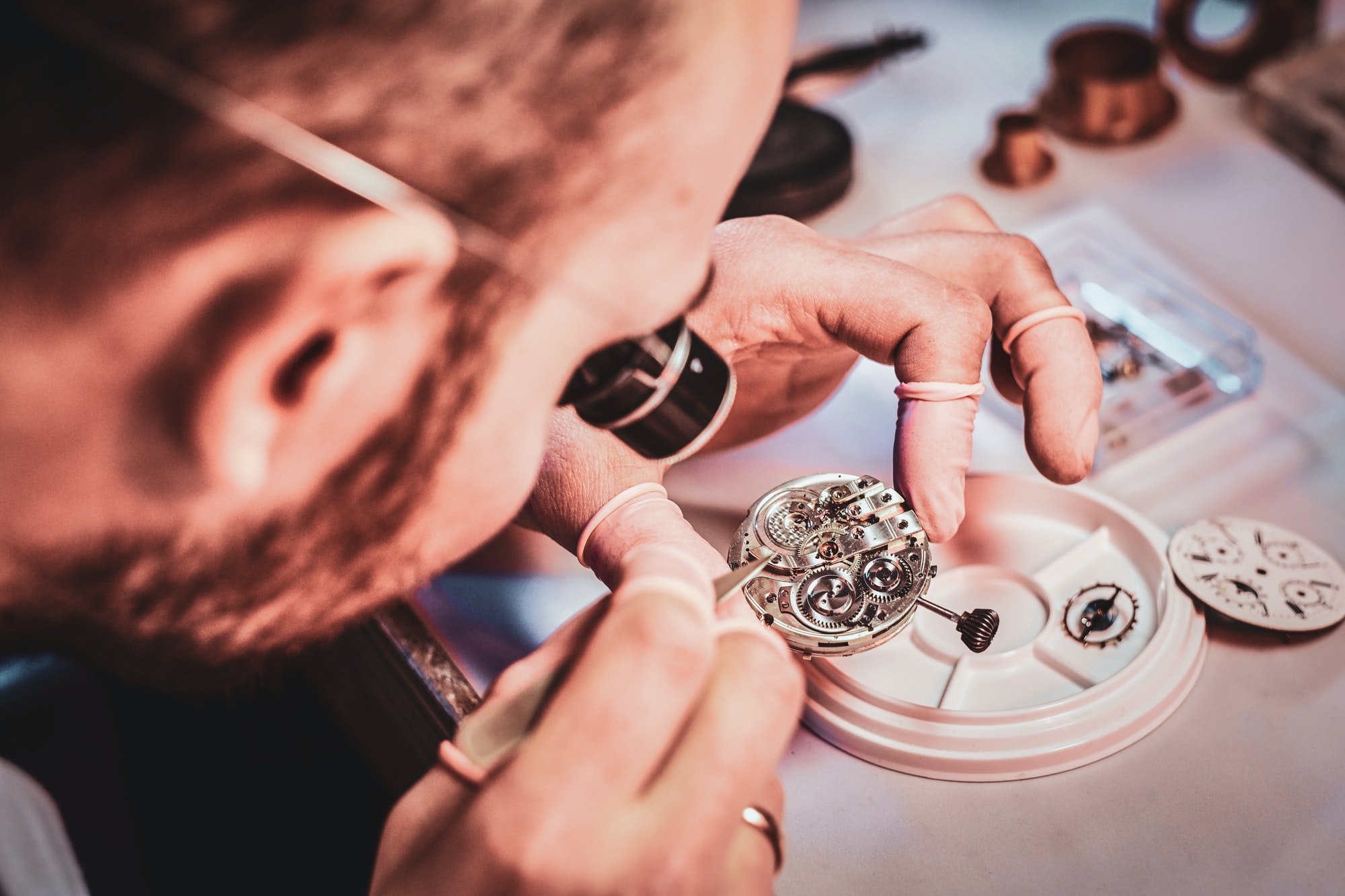 Mature clockmaster is fixing old watch for a customer at his busy repairing workshop